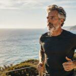 Longevity Story | Come rimanere giovani e rallentare l'invecchiamento — uomo maturo con barba grigia corre su un sentiero costiero al tramonto